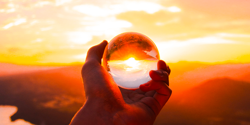 vita-evidenza una mano tiene una sfera trasparente attraverso la quali si vede il tramonto all'orizzonte