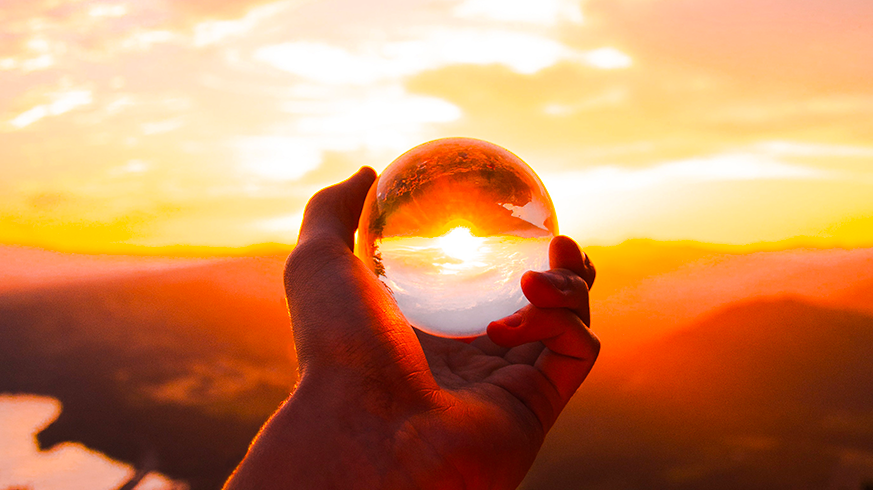 una mano tiene una sfera trasparente attraverso la quali si vede il tramonto all'orizzonte